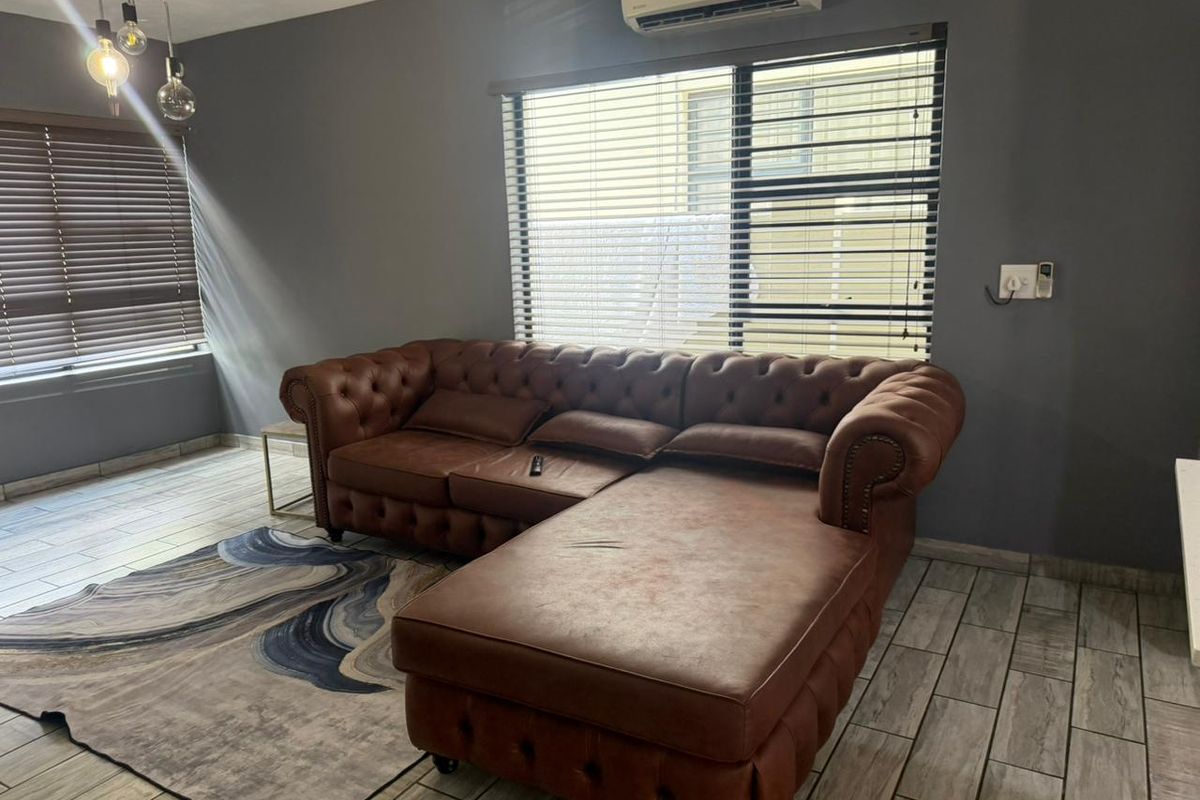 A well-lit living room featuring modern tiled flooring, venetian blinds, and a wall-mounted split-system air conditioner.