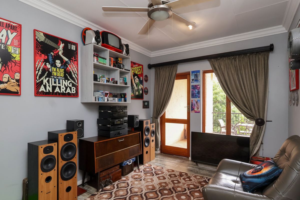 A living room featuring laminate flooring, crown molding, a ceiling fan, and direct access to an outdoor balcony through a timber-framed glass door.