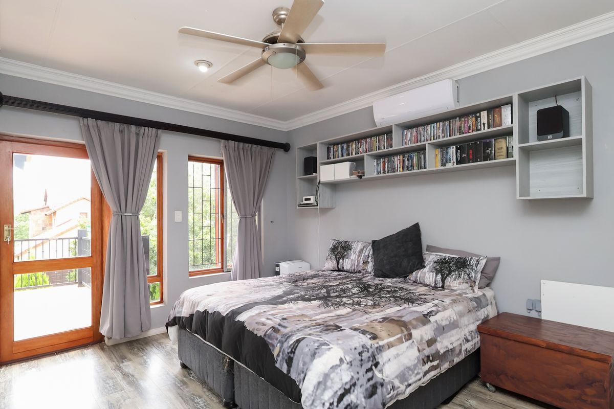 A well-maintained bedroom featuring laminate flooring, a ceiling fan, split-system air conditioning, and custom built-in shelving with direct access to an outdoor balcony.