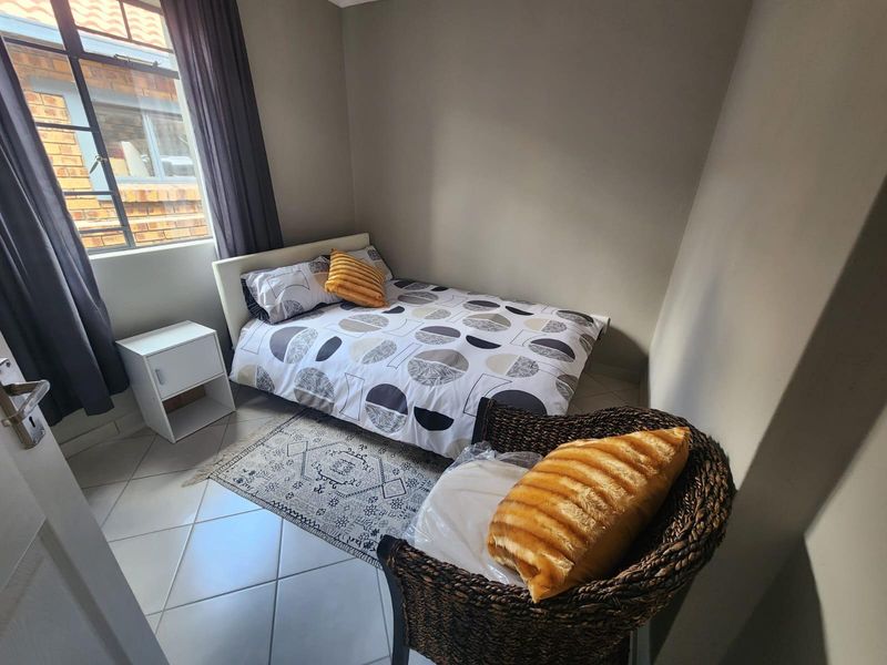 A compact bedroom featuring neutral wall tones, tiled flooring, and a steel-framed window providing natural light.