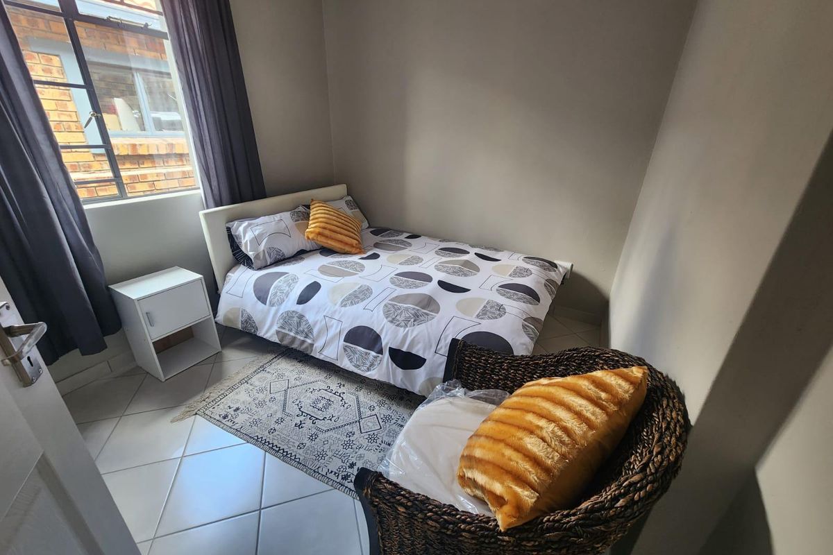 A compact bedroom featuring neutral wall tones, tiled flooring, and a steel-framed window providing natural light.