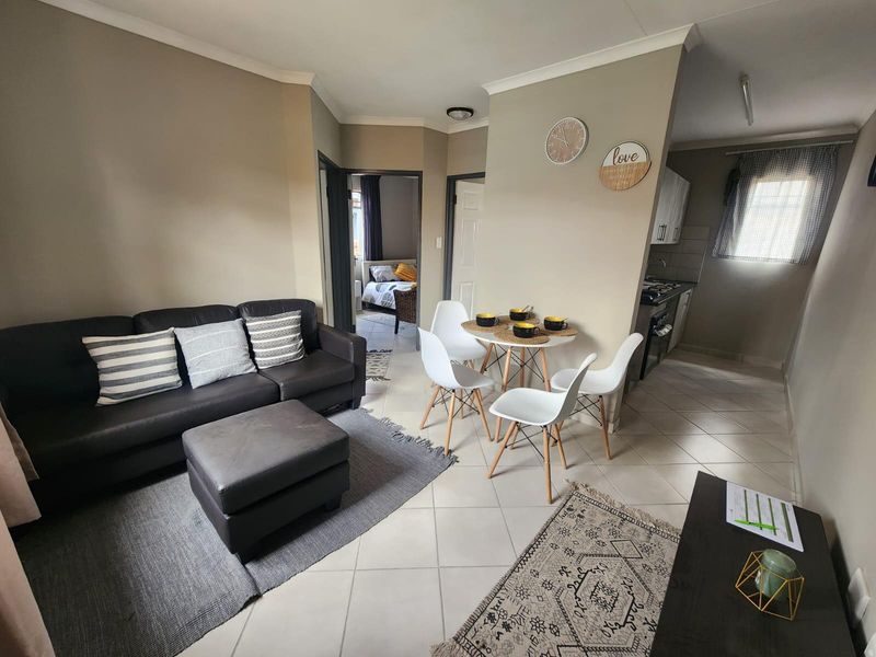 An open-plan living and dining area featuring tiled flooring, neutral wall tones, and a compact kitchen space with built-in cabinetry and appliances.
