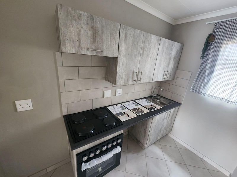 A compact, modern kitchen featuring wood-look cabinetry, a built-in electric oven and hob, subway tile backsplash, and a stainless steel sink.