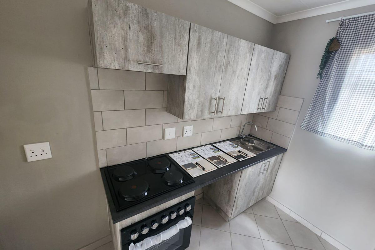 A compact, modern kitchen featuring wood-look cabinetry, a built-in electric oven and hob, subway tile backsplash, and a stainless steel sink.