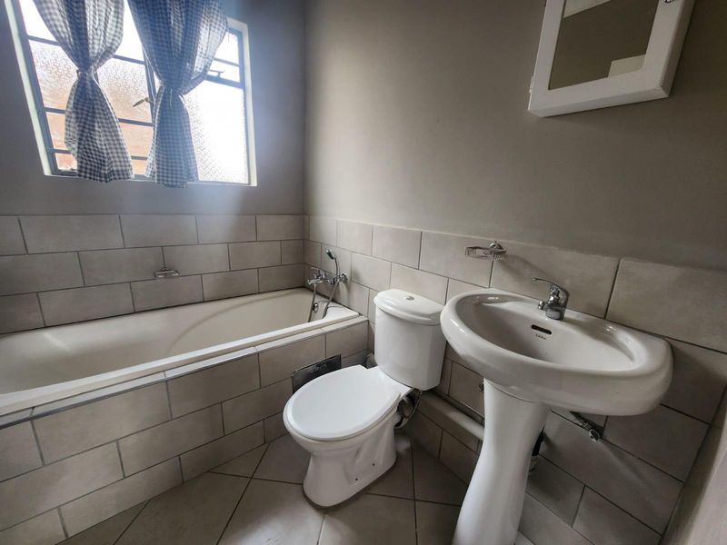 A functional bathroom featuring a built-in bathtub, pedestal washbasin, and toilet with neutral wall and floor tiling.