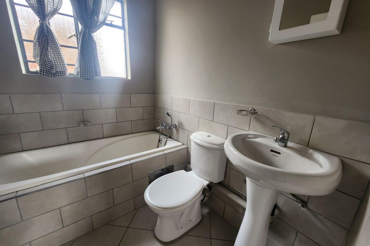 A functional bathroom featuring a built-in bathtub, pedestal washbasin, and toilet with neutral wall and floor tiling.