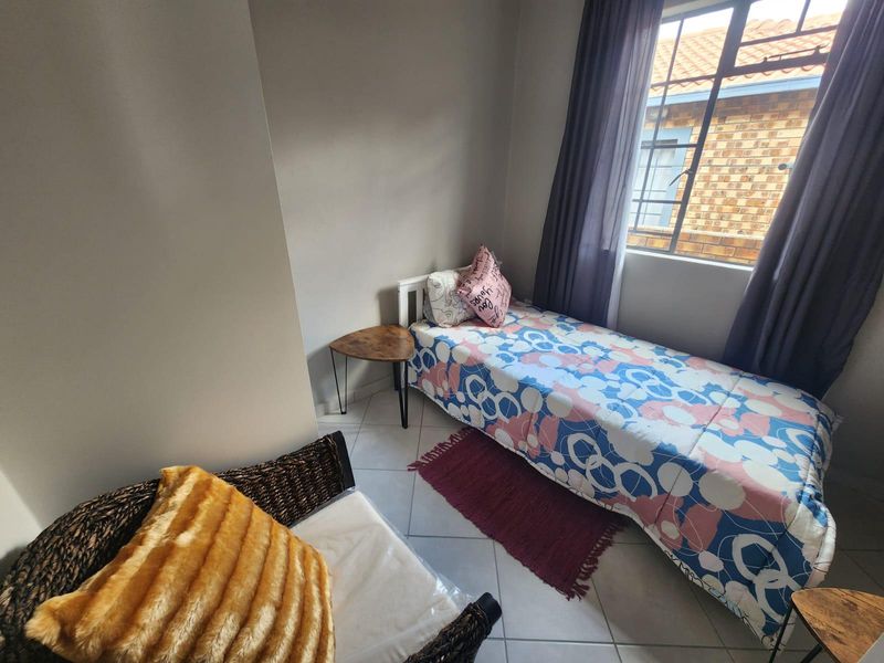 A compact bedroom featuring tiled flooring and a window with security bars, providing natural light and a functional layout.