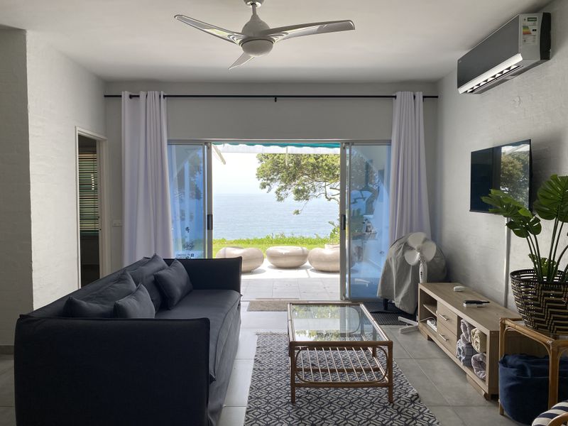 Bright living room featuring tiled floors, a ceiling fan, and split-system air conditioning, with large sliding glass doors opening to a scenic ocean view.