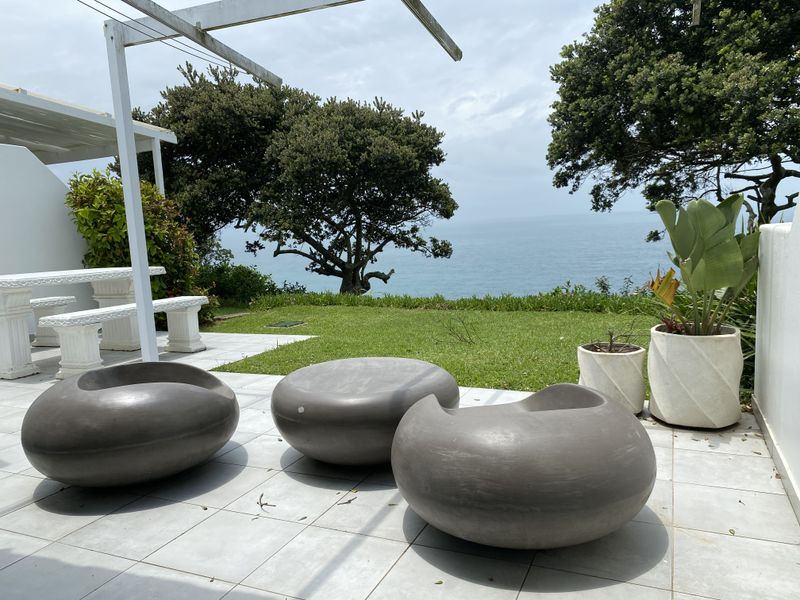 A paved outdoor patio area featuring a pergola structure, overlooking a lush garden with expansive ocean views.