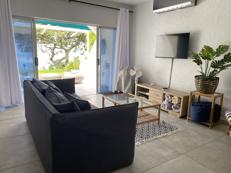 A bright living room featuring large sliding glass doors that open to an outdoor patio area, complete with tiled flooring and a wall-mounted air conditioner.