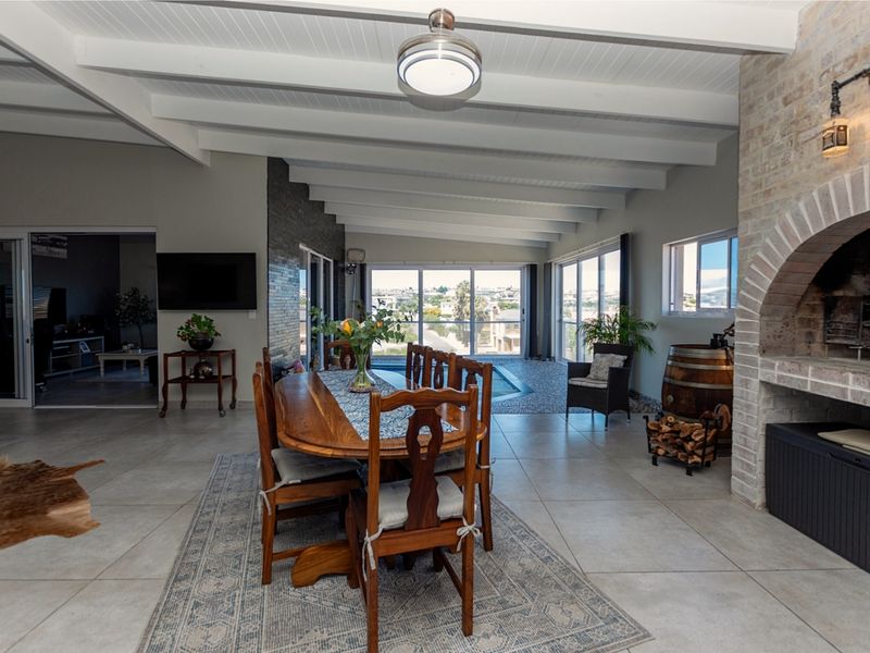 Spacious open-plan living and dining area featuring exposed beam ceilings, a classic brick fireplace, and large sliding doors leading to the outdoor pool area.