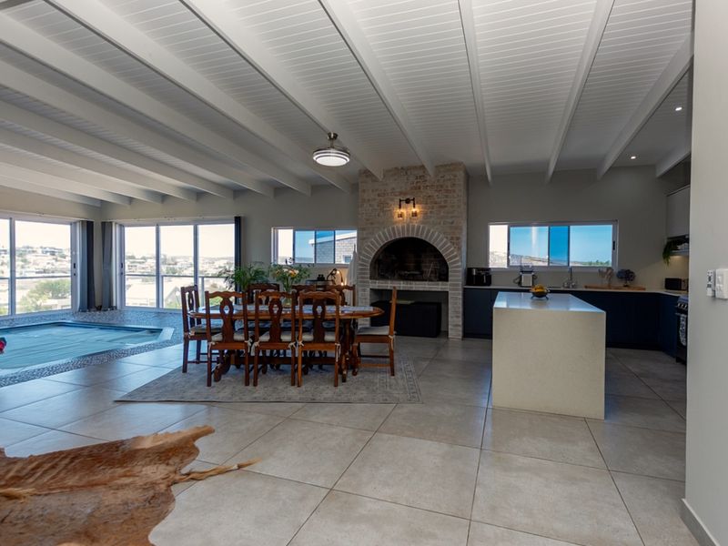 Spacious open-plan living area featuring a modern kitchen with island, brick fireplace, exposed beam ceilings, and direct access to an indoor pool.