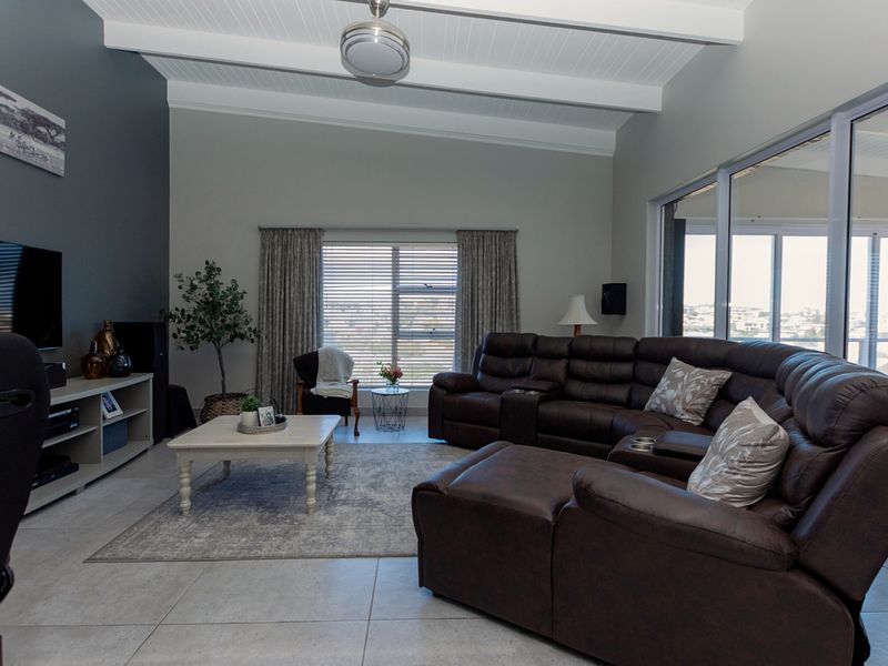 Spacious living room featuring vaulted ceilings with exposed beams, tiled flooring, and large sliding glass doors that provide ample natural light.
