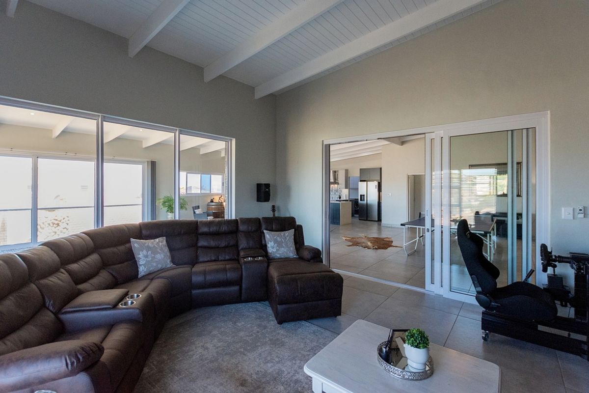 Spacious living room featuring a vaulted ceiling with exposed beams, tiled flooring, and large sliding glass doors providing ample natural light and seamless flow.