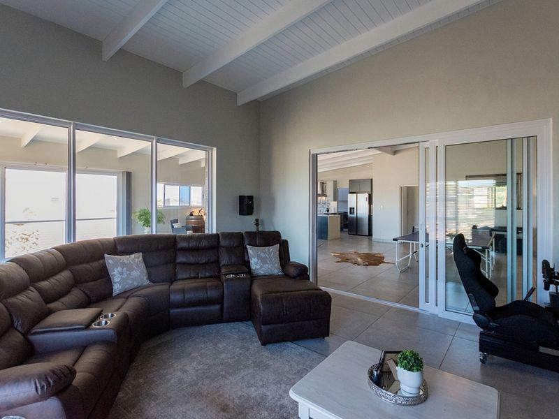 Spacious living room featuring a vaulted ceiling with exposed beams, tiled flooring, and large sliding glass doors providing ample natural light and seamless flow.
