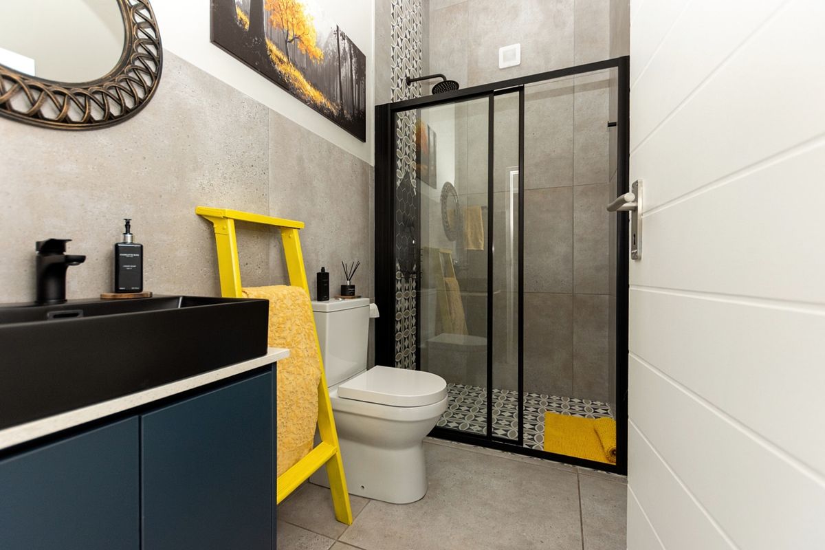 Modern bathroom featuring a sleek black-framed shower enclosure, contemporary vanity with countertop basin, and stylish grey tiled finishes.