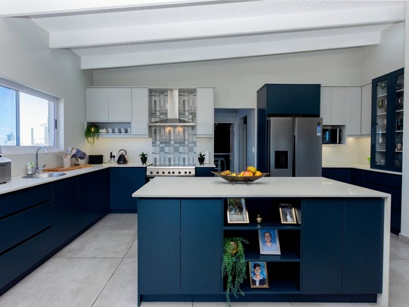 Modern kitchen featuring a central island, navy and light grey cabinetry, quartz countertops, stainless steel appliances, and exposed white ceiling beams.