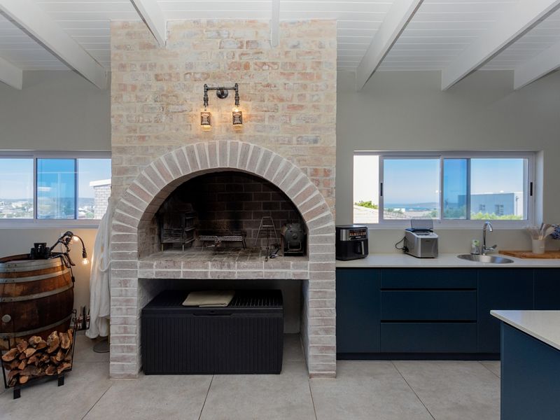 Modern kitchen featuring a prominent built-in brick fireplace, dark blue cabinetry, stainless steel sink, and exposed beam ceilings with tiled flooring.