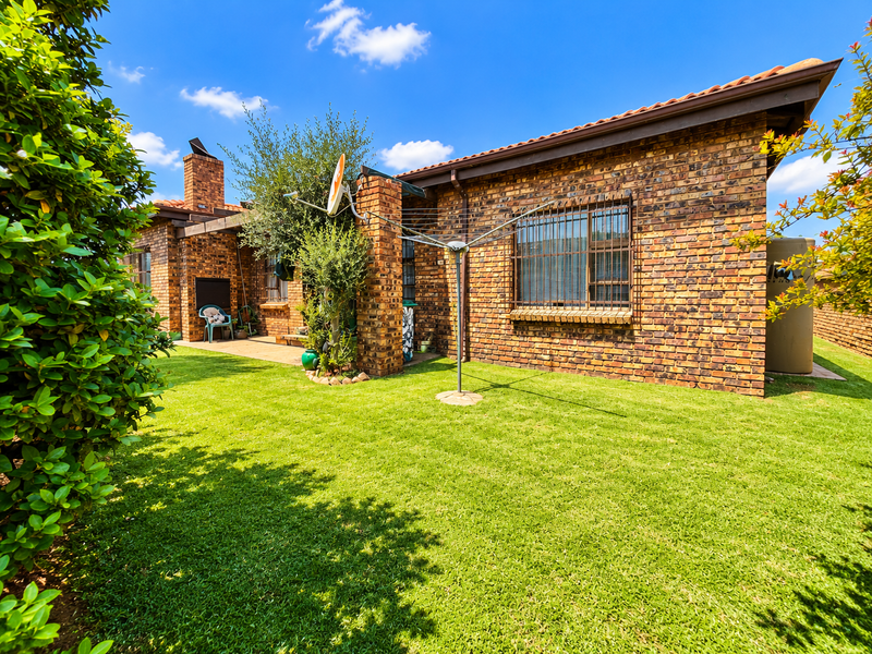 Rear view of the townhouse featuring a face brick facade, tiled roof, security bars on windows, and a well-maintained lawn with a paved patio.