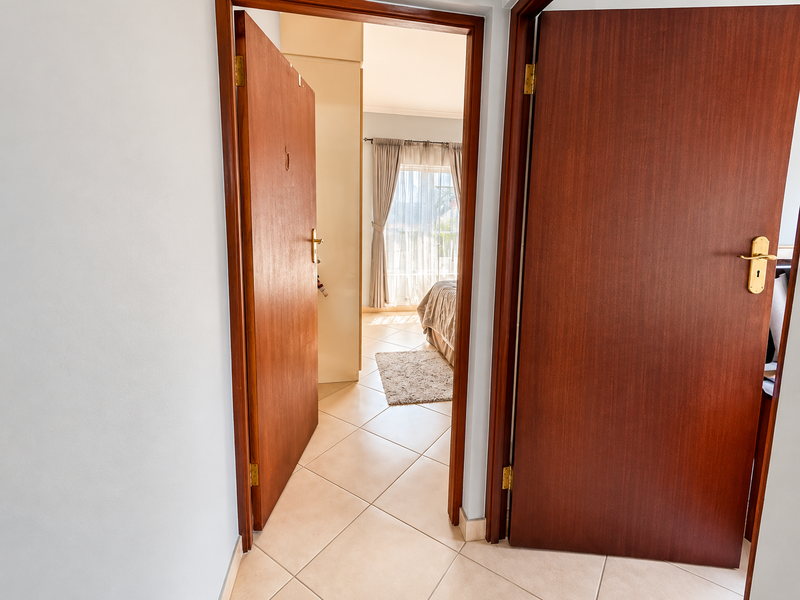 A bright hallway featuring tiled flooring and solid wooden doors, providing access to an adjacent bedroom with natural light.