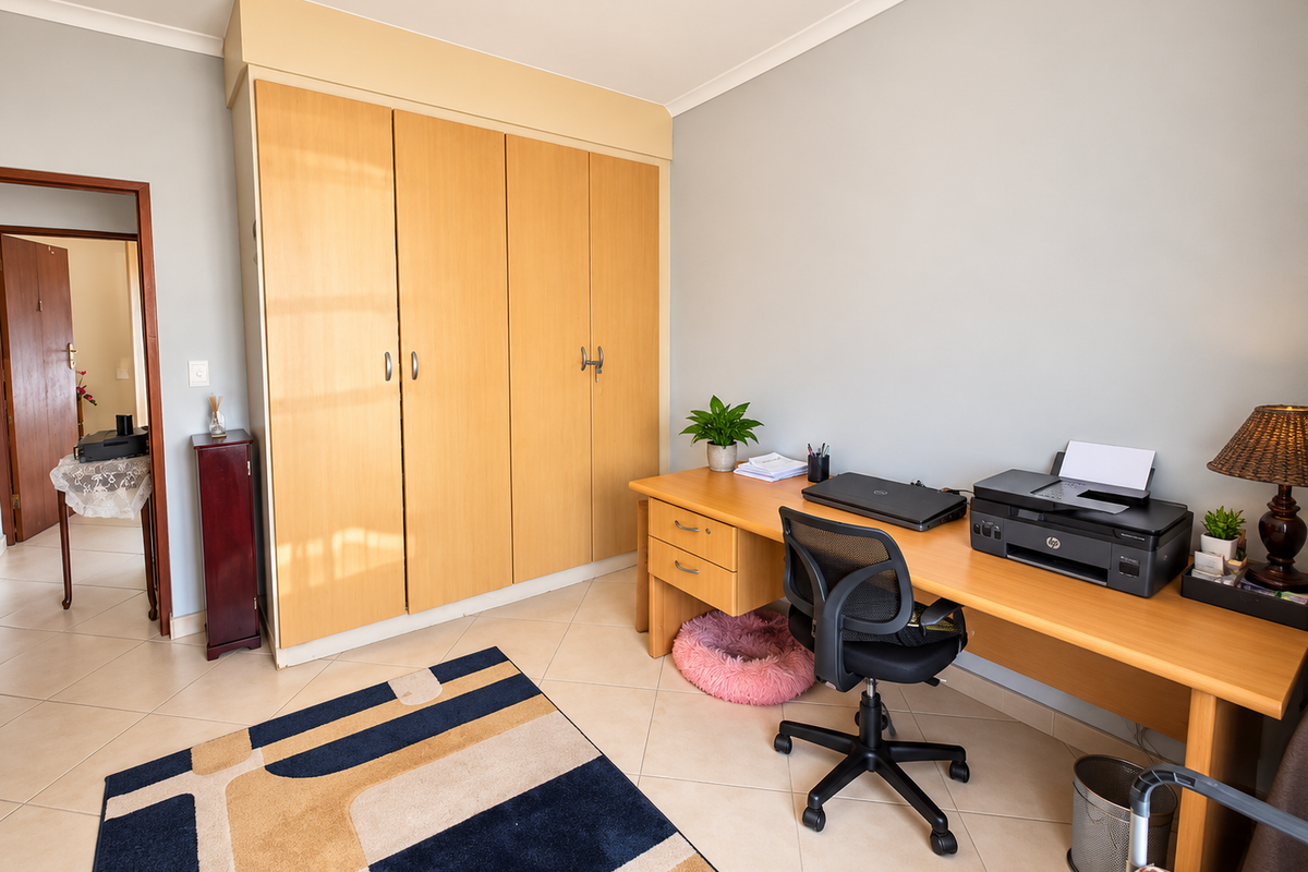 A bedroom featuring built-in wooden cupboards, tiled flooring, and coved ceilings, currently utilized as a home office space.