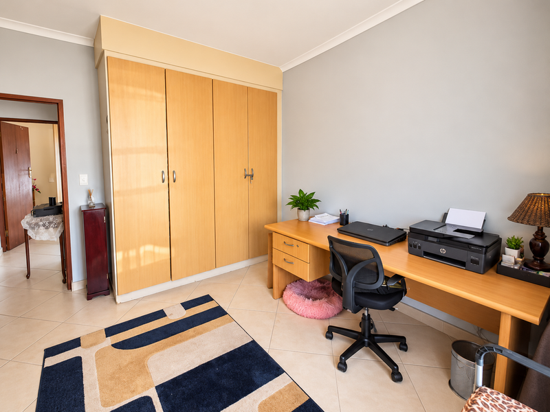 A bedroom featuring built-in wooden cupboards, tiled flooring, and coved ceilings, currently utilized as a home office space.