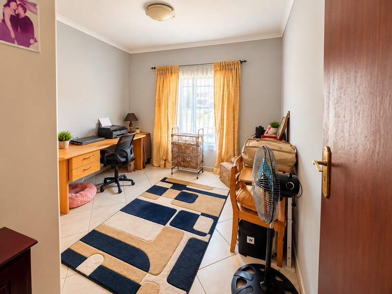A functional home office space featuring neutral wall tones, ceramic tiled flooring, and natural light through a window with curtain fixtures.