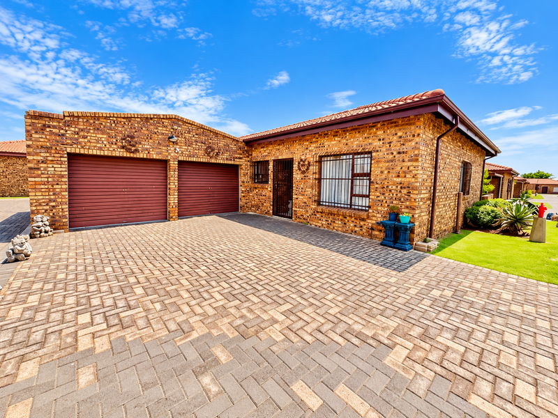 A well-maintained townhouse featuring a face brick exterior, double garage, and a neat paved driveway with secure window bars.