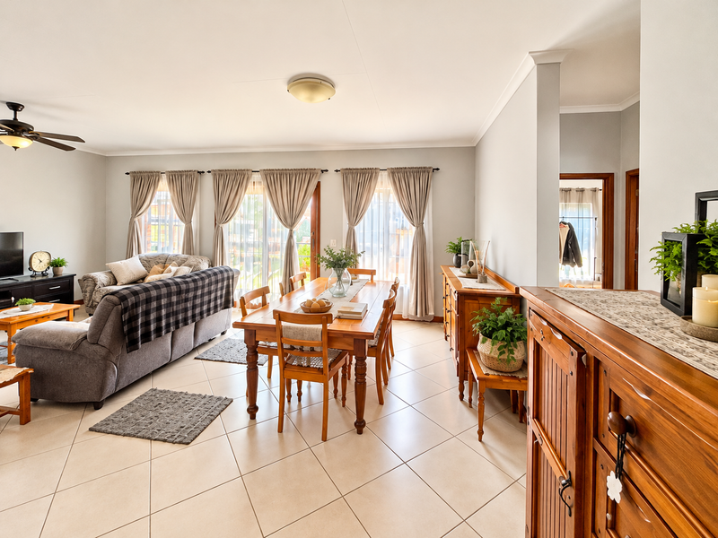Spacious open-plan living and dining area featuring neutral ceramic floor tiles, large sliding glass doors for natural light, and a ceiling fan.