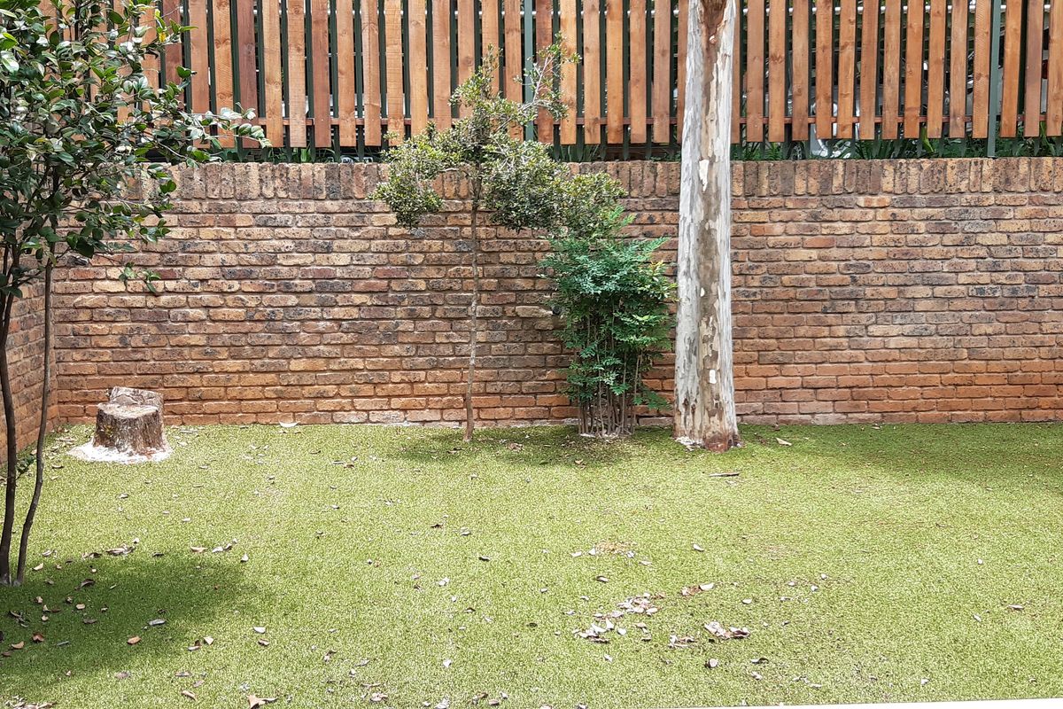 A private rear courtyard featuring a low-maintenance artificial lawn, enclosed by a face brick boundary wall and timber slat fencing.