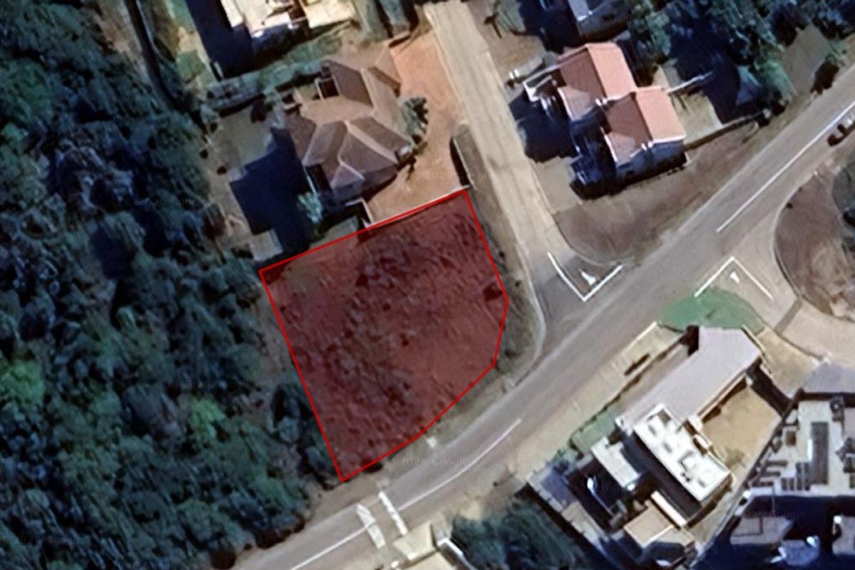 An aerial view of a vacant residential plot outlined in red, situated in a developed neighborhood with established road access and surrounding vegetation.