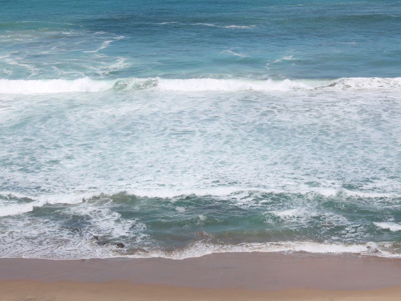 A scenic view of the ocean waves crashing onto the sandy beach.