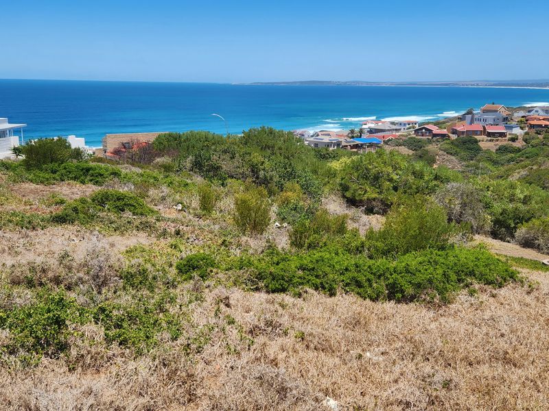 A vacant residential plot offering expansive coastal and ocean views, situated in a developed neighborhood with established vegetation.
