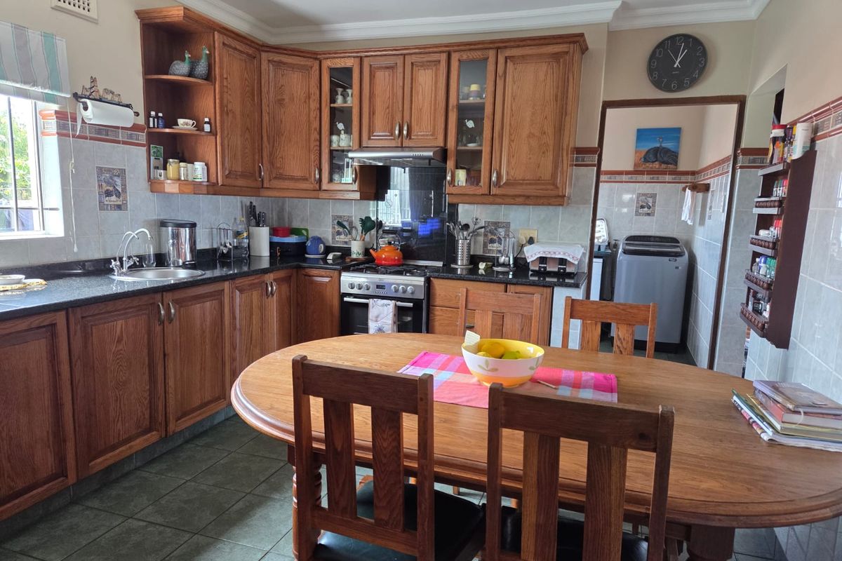A functional kitchen featuring timber cabinetry, granite countertops, and a tiled splashback, with an adjacent laundry area visible through the doorway.
