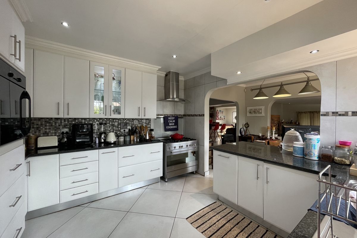 Modern kitchen featuring white cabinetry, granite countertops, stainless steel appliances, and a mosaic tile backsplash, seamlessly flowing into the adjacent living area.