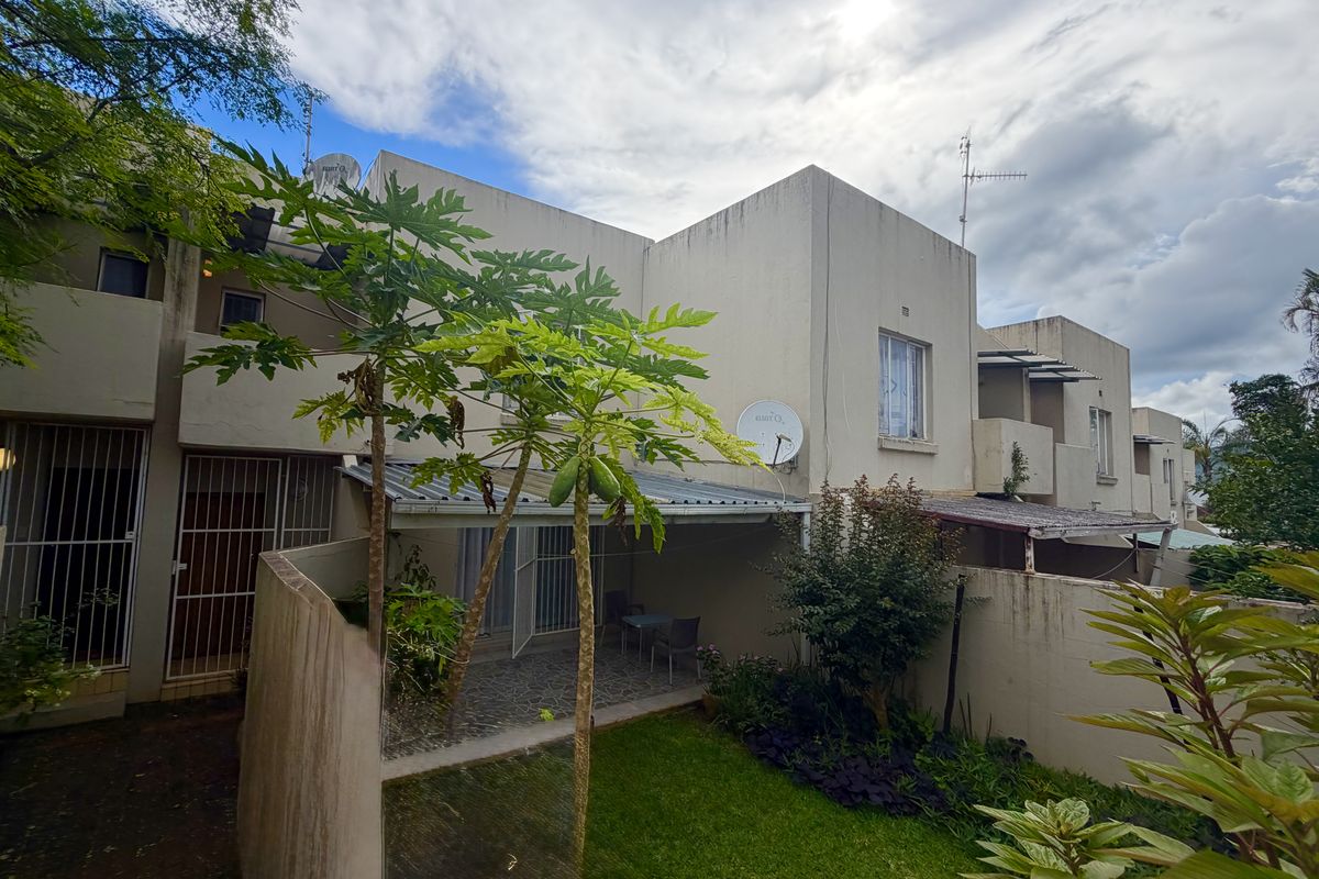 Rear view of the townhouse featuring a small private garden, a covered patio area, and security gates on the ground floor access points.