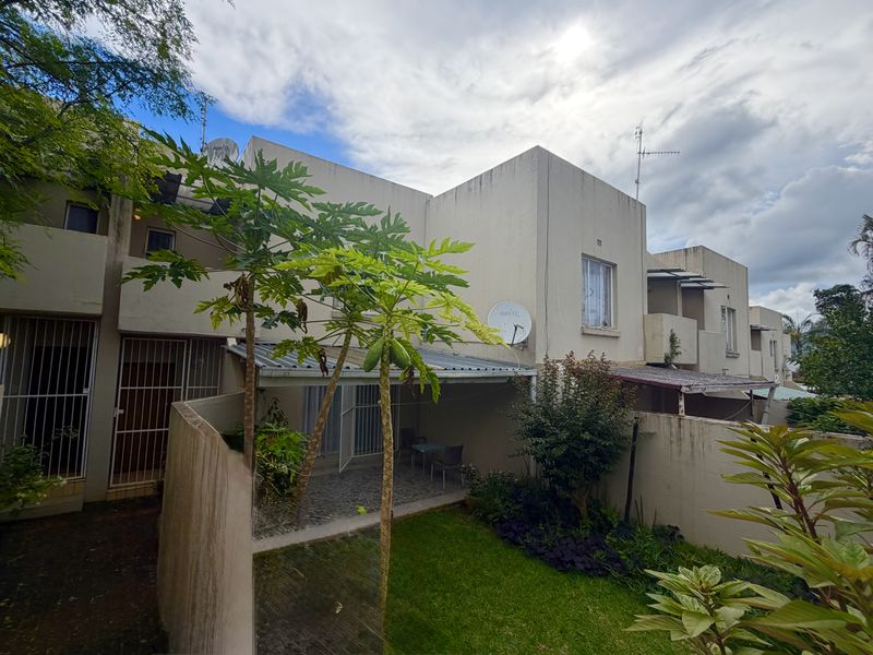 Rear view of the townhouse featuring a small private garden, a covered patio area, and security gates on the ground floor access points.