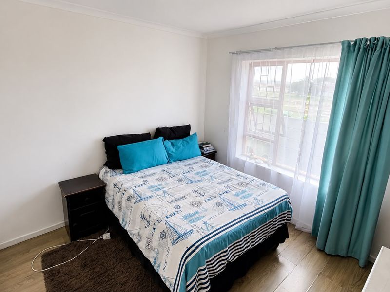 A well-maintained bedroom featuring laminate flooring, a built-in wardrobe, and a window fitted with security bars and curtains.