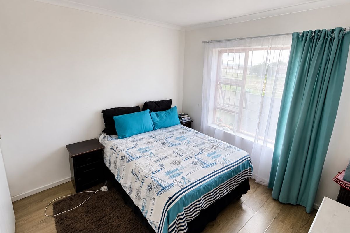 A well-maintained bedroom featuring laminate flooring, a built-in wardrobe, and a window fitted with security bars and curtains.