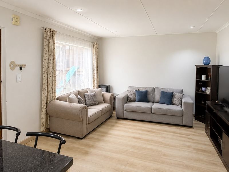 A bright and well-maintained living room featuring light-toned laminate flooring and recessed ceiling lighting, creating a comfortable and inviting atmosphere.