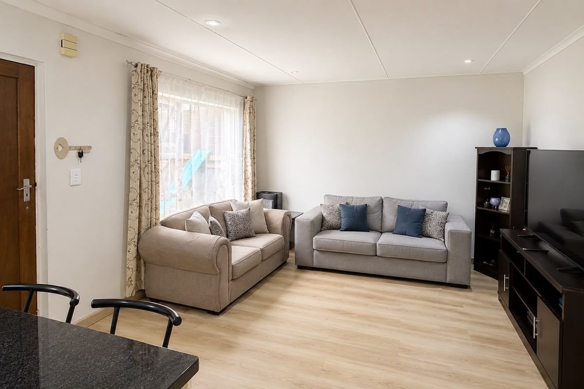 A bright and well-maintained living room featuring light-toned laminate flooring and recessed ceiling lighting, creating a comfortable and inviting atmosphere.