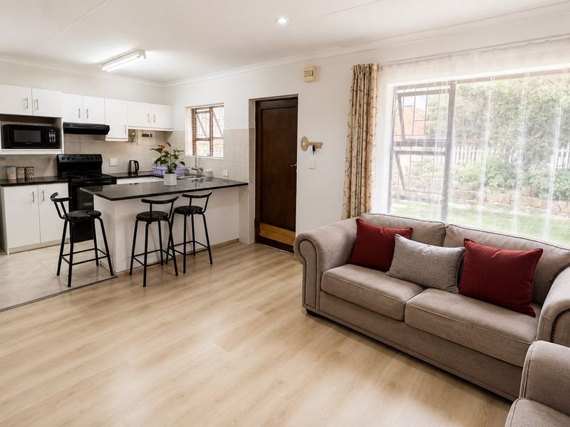 An open-plan living and kitchen area featuring modern laminate flooring, a breakfast bar, and direct access to the garden through a large window.