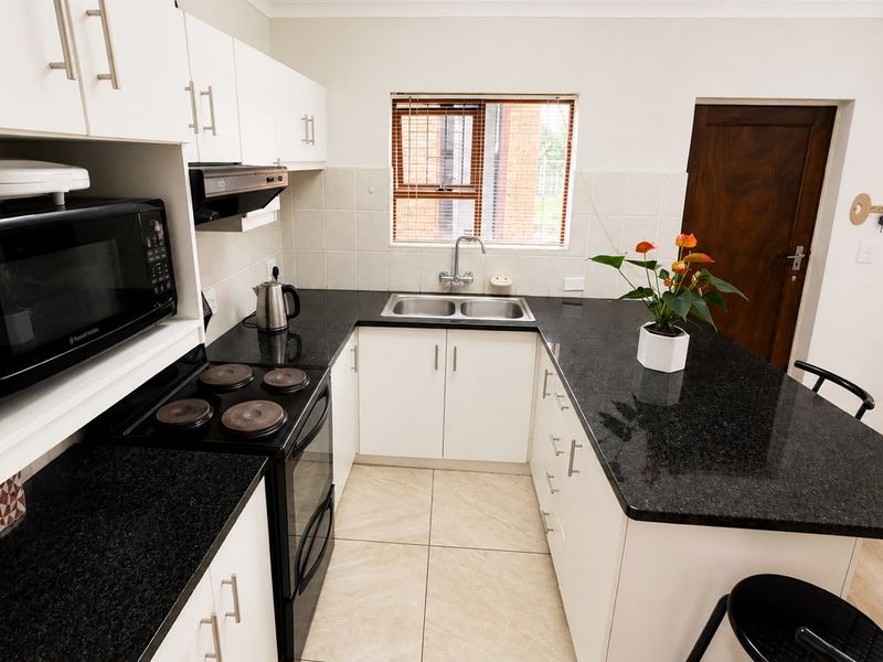 A functional kitchen featuring white cabinetry, contrasting black granite countertops, a double basin sink, and tiled flooring with a practical layout.
