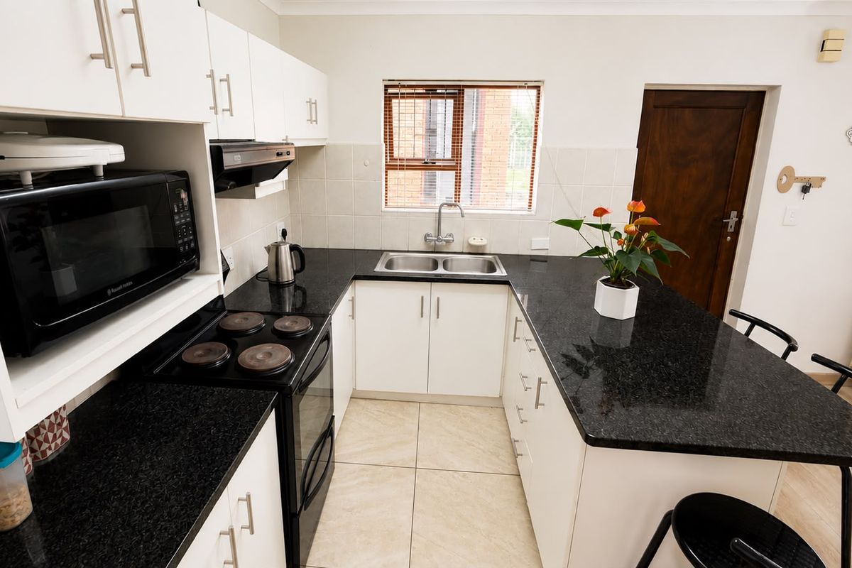 A functional kitchen featuring white cabinetry, contrasting black granite countertops, a double basin sink, and tiled flooring with a practical layout.