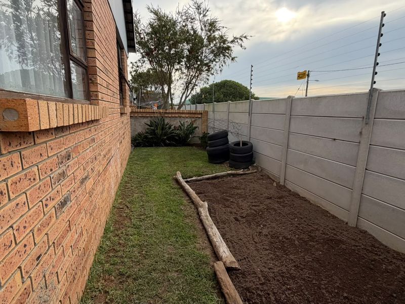 A side garden area featuring a face brick exterior wall, a precast concrete boundary wall with electric fencing, and a small lawn section.
