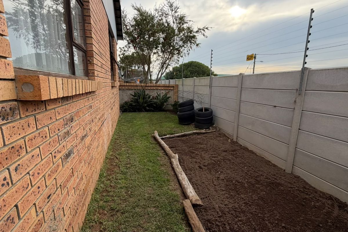 A side garden area featuring a face brick exterior wall, a precast concrete boundary wall with electric fencing, and a small lawn section.