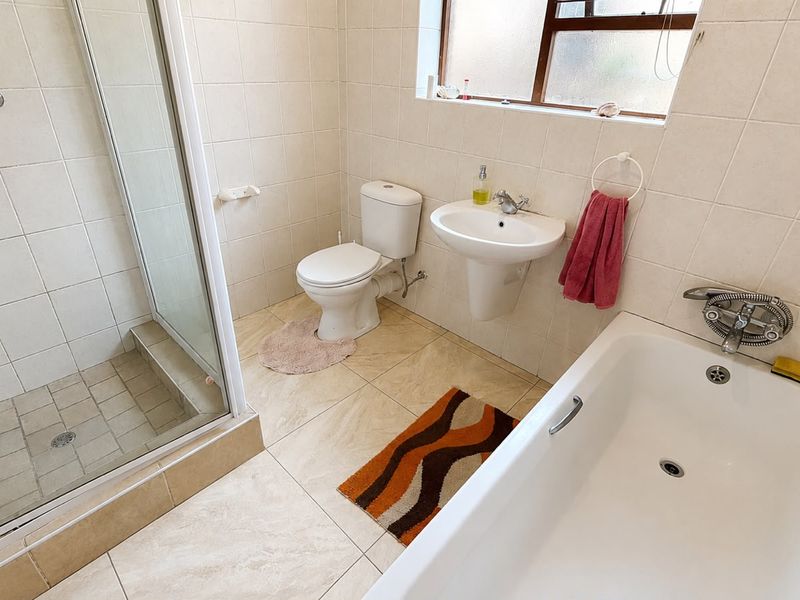 A functional bathroom featuring a shower enclosure, pedestal basin, toilet, and bathtub with neutral wall and floor tiling.