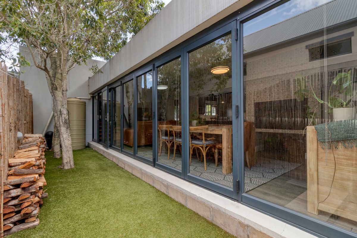 Rear exterior view featuring modern aluminium stacker doors opening onto a landscaped garden area with artificial lawn and a water tank.