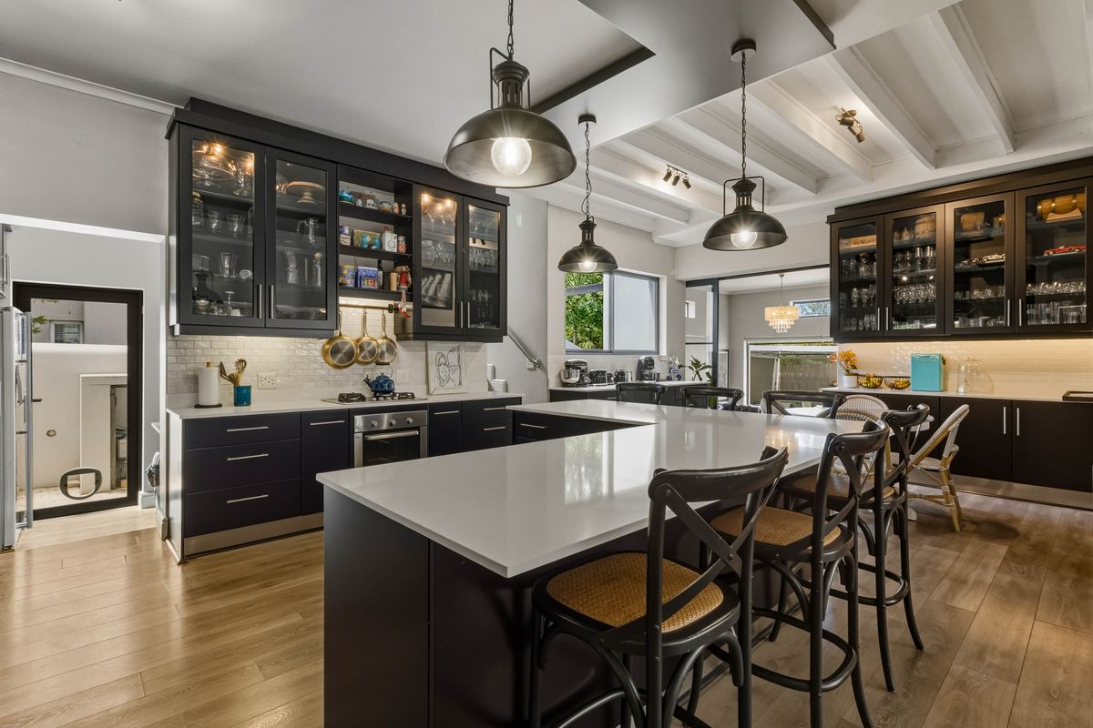 Modern kitchen featuring dark cabinetry, quartz countertops, a large central island, subway tile backsplash, and exposed beam ceilings with stylish pendant lighting.