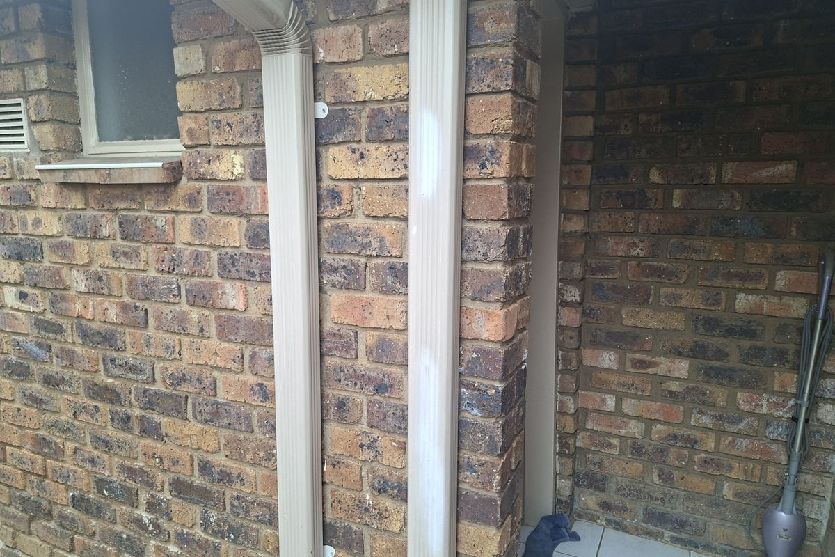 A view of the exterior rear brick wall featuring a downpipe and tiled patio area.